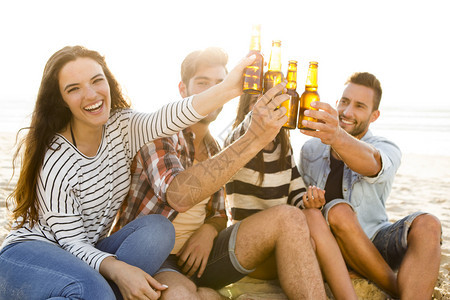 混合朋友在沙滩玩得开心喝冷啤酒的精女图片