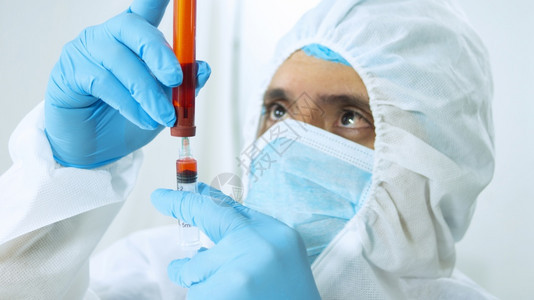医院蓝色的化学身穿生物防护服面罩和蓝色手套的拉丁医生在白色背景上用注射器在试管中抽取血液样本的特写视图身穿生物防护服面罩和蓝色手图片