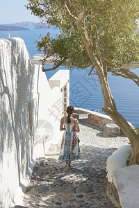 裙子在圣桑托里尼Oia村与欧洲Santorini夏季目的地中海在楼梯上行走的女游客背面太阳镜观光图片