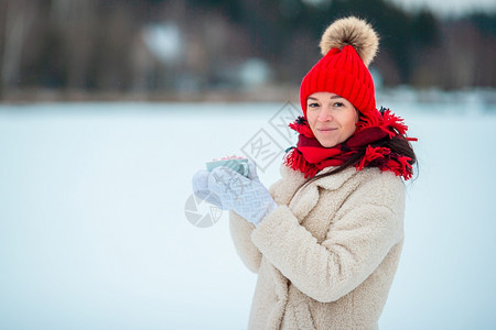 戴着红帽的快乐女孩喝着热饮咖啡和棉花糖手放在户外的白杯里拿铁热可口图片