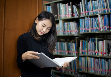 背靠图书馆书架看书的亚洲女孩图片