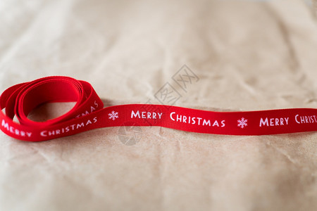 最佳问候写有圣诞快乐题字的红丝带在工艺纸上展开装饰图片