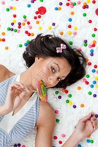 年轻的拉丁女人躺在乌云上像地板一样在吃棒糖的多彩泡金球之间拉丁裔蓝色的摄影图片