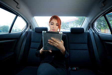 用平板电脑在车里的年轻商业女青药片司机座位图片