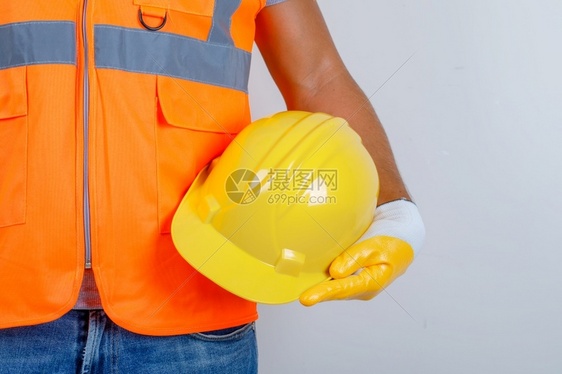 工程师快乐的帽子身穿制服牛仔裤手握戴头盔的套前视图片
