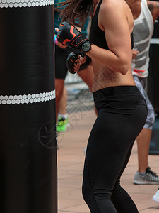 人们穿黑色运动服体操健身的年轻女孩拳击袋练习肌肉图片