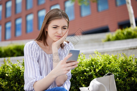 在校园花坛旁坐着玩手机的不开心女孩图片