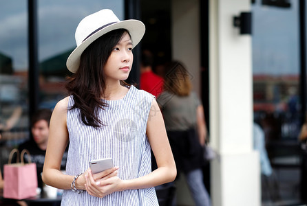成人亚洲年轻女手持智能机站在市内户外咖啡馆门前的户外背景在工作的人与技术城市生活方式电话用户一起在外工作商业图片