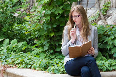 坐在被常春藤覆盖的大楼外阅读日记本的女孩图片
