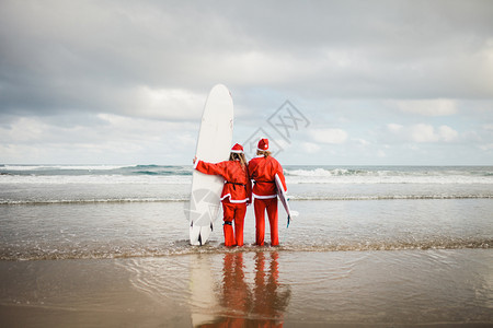 两个在海滩冲浪时打扮成圣诞老人的冲浪者天气快乐的帽子图片