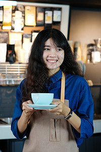 在咖啡馆柜台背景小商业主食品和饮料业面笑脸的可支配咖啡杯中持有一次咖啡杯的年轻女咖啡会在室内制服年轻的图片