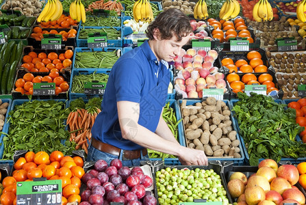 创建在一家商店里各种新鲜水果和蔬菜箱中工作的一个绿色杂货店员男人柜台图片