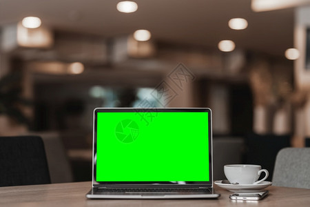 在咖啡店背景的桌子上用空屏幕咖啡杯和智能手机抽装笔记本电脑绿色屏幕在线的设计师空图片