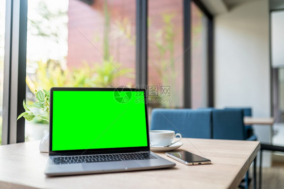 工作场所桌面嘲笑在咖啡店背景的桌子上用空屏幕咖啡杯和智能手机抽装笔记本电脑绿色屏幕图片