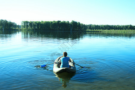 穿蓝色T恤衫的女孩坐在橡皮船上大湖排行游泳多云的池塘镇图片