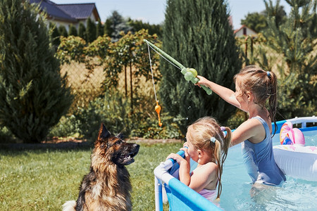 放松微笑孩子们用钓鱼竿玩具站在家庭花园的游泳池里和狗玩耍孩子们在夏日阳光明媚的子里一起玩耍夏天图片