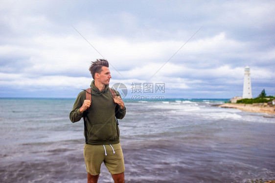 岩石在风暴海岸附近的旅游者望着灯塔双人步行到灯塔快乐的男人图片