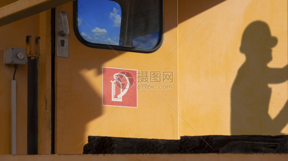 机械在车库检查和维修期间火车头门上有红色灭火器标志的侧边视线在橙色火车墙表面有阳光和工人的影子并在车库内进行检查和维护头盔修理图片