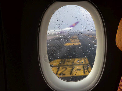 在停跑道上的客机窗户外玻璃上落下的雨滴在玻璃面上水气泡空图片