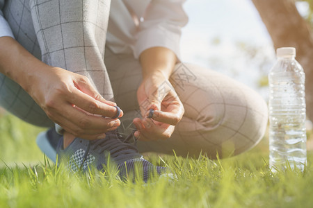 亚洲人早上在公共园的绿草和水瓶上搭着妇女手绑绳索运动鞋放在绿色草地和水瓶上慢跑者女孩图片