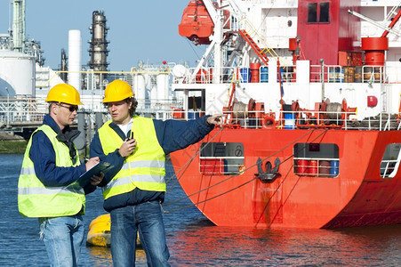 两艘码头在工作身穿安全背心手戴硬帽子坐在石化港的红消防船顶上严厉火助手图片
