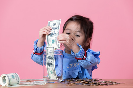 经济小女孩把钞票放进一个清晰的玻璃罐子里钱储蓄概念人们银行业图片