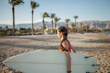年轻女子带着冲浪板在海滩上行走活动等待棕榈图片