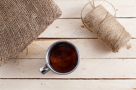 茶叶旁边的木制背景茶杯是画布和一连串的线条在茶叶旁边的木制背景上有茶的铁旧杯子下午热的线程图片