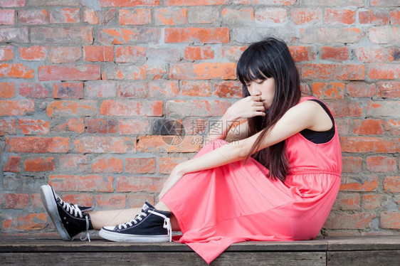年轻的经过沉思坐在红砖墙边年轻亚洲妇女感到沮丧和悲伤图片