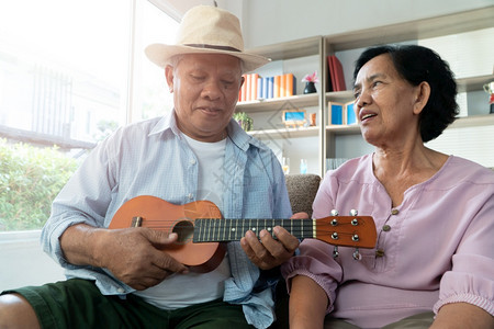 拥抱尤克里微笑快乐的亚洲老年情侣在玩乌鲁列尔语在家里一起唱歌幸福退休后老年人的生活概念幸福退休后老年人的生活概念图片