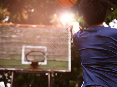 一个十几岁的男孩拿着篮球把扔进户外场的环圈里闲暇持有图片