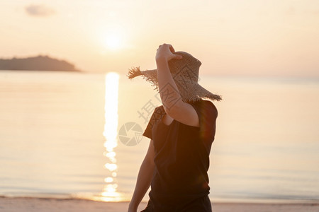 穿着黑色T恤衫和草帽的男子在海滩上享受美丽的日出或落早晨稻草天空图片