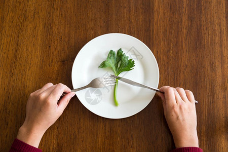 低的重量饮食概念空白盘上一种绿色蔬菜女人手放在木桌上芹菜放在木桌上健康顶视图饮食概念芹菜健康桌子图片