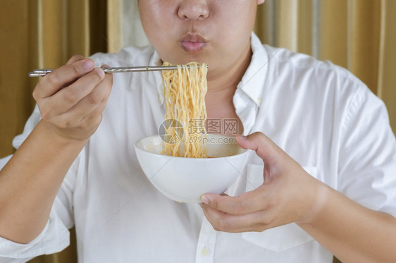 人身穿白衬衫的亚洲人加上身高相近的亚洲人用银筷子在家里吃快面和吹热的泰国图片