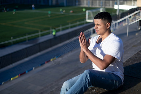 优胜者希望成人年轻在祈祷时闭着眼睛坐在体育场的露天运动机上图片