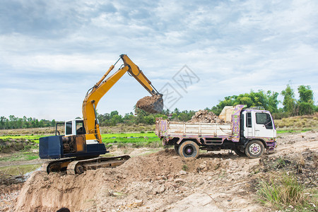 工作桶黄色挖掘机将土壤装入建筑工地的倾卸卡车中活动图片