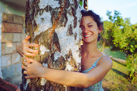 美丽的女孩士春秋天在后院的夏装女青年盛拥抱树干和享受大自然快乐的笑容图片