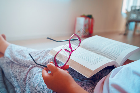 尽管紧贴在坐家庭后视的地板上阅读或学习时持有书本和眼镜的女孩或妇中间部者一种专业的图片