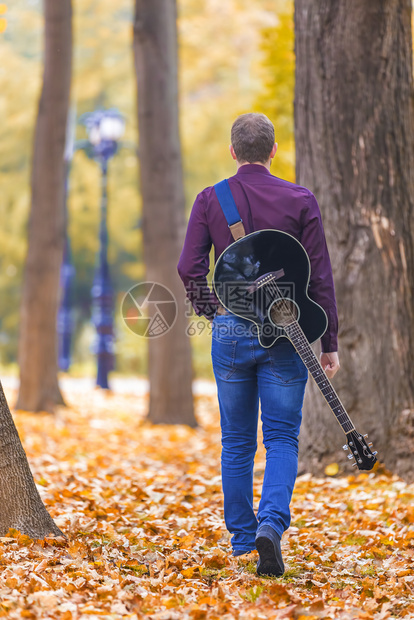 自然叶子男人年轻带着音响吉他在城市公园的树叶上行走关注吉他图片