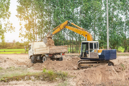 液压倾倒黄色挖掘机将土壤装入建筑工地的倾卸卡车中沙漠图片