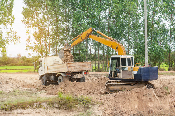 液压倾倒黄色挖掘机将土壤装入建筑工地的倾卸卡车中沙漠图片