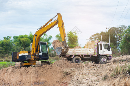 机械运输黄色挖掘机将土壤装入建筑工地的倾卸卡车中力量图片