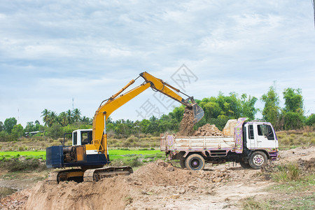 倾倒机械进入黄色挖掘机将土壤装入建筑工地的倾卸卡车中图片