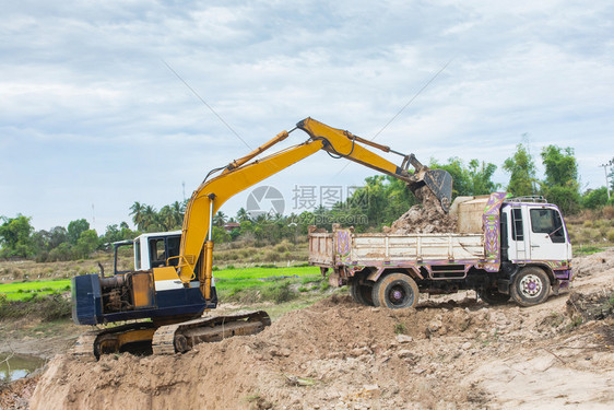自然地球黄色挖掘机将土壤装入建筑工地的倾卸卡车中辆图片