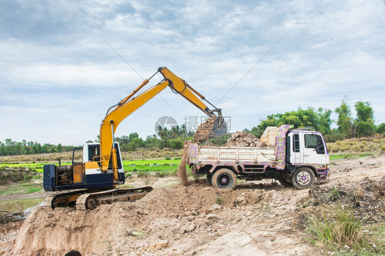 自卸车污垢伊拉克黄色挖掘机将土壤装入建筑工地的倾卸卡车中图片