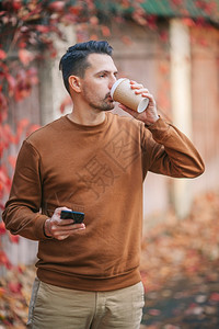自然男人在秋天公园喝咖啡的男青年在秋日公园户外喝咖啡的男青年微笑图片