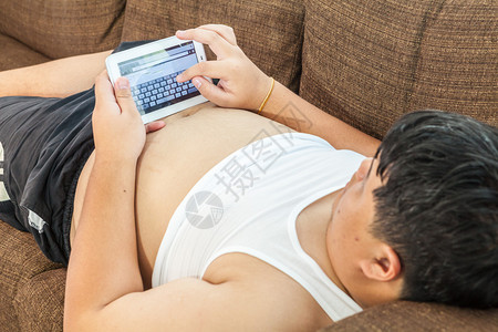 亚洲胖子在沙发里放松家有平板电脑亚洲人偏僻的快乐图片