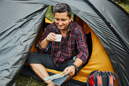 暑假期间男子在露营帐篷中放松男子持有同时计划下一次出行积极在与自然相近的户外度假营地生活概念喝野营松弛图片