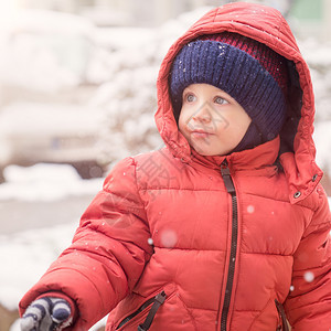 尽管婴儿男孩在下雪时看着空虚满身是红冬夹克和羊毛帽贴近白色的降雪图片