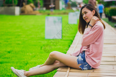 坐着幸福绿色在竹桥上身穿粉红衬衫的女人图片